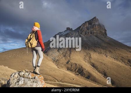 Porträt von der Rückseite eines Reisenden in einer Jacke mit einer Mütze und einem Rucksack steht vor dem Hintergrund einer epischen Landschaft mit Felsen Stockfoto