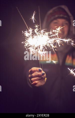 Lächelndes Mädchen hält ein funkelndes Mädchen in der Hand, Neujahr, draußen Stockfoto