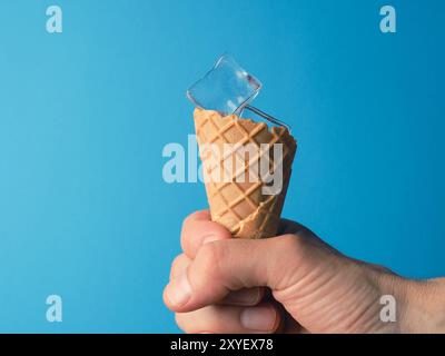 Hand ein Eis Kegel mit Eiswürfel auf blauem Hintergrund, heißen Sommer Konzept Stockfoto