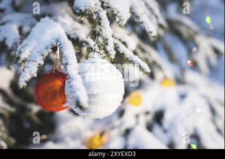 Nahaufnahme eines Weihnachtsspielzeugs auf einem schneebedeckten, lebhaften Baum im Winterwald auf dem Hintergrund von Lichtern Stockfoto