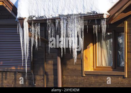 Im Winter oder Frühling Hintergrund von hellen Eiszapfen im Sonnenlicht auf dem Dach von Schnee bedeckt Chalet aus Holz Stockfoto