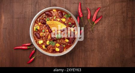 Chili con carne mit Paprikas und Nacho Chips, Overhead Panorama-aufnahme auf einem dunklen Holzmöbeln im Landhausstil Hintergrund mit einem Platz für Text Stockfoto