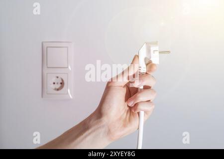 Weißer Stecker mit Kabel in männlicher Hand, bereit zum Anschließen. Energiekonzept Stockfoto