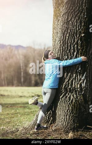 Schöne blonde Mädchen mit in Sportbekleidung ist einen Baum umarmen Stockfoto