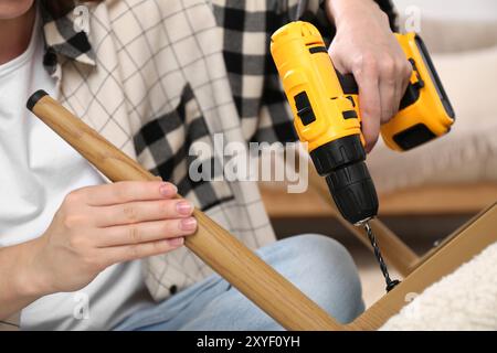 Frau mit elektrischem Schraubenzieher, der den Sessel im Zimmer zusammenstellt, Nahaufnahme Stockfoto