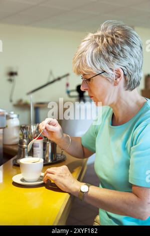 Frau sitzt an einer Theke und rührt ihren Kaffee mit einem Löffel um Stockfoto