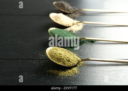 Verschiedene Superfood-Pulver in Löffeln auf schwarzem Holztisch, Nahaufnahme Stockfoto