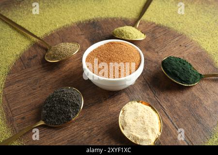 Verschiedene Superfood-Pulver in Löffeln und Schüsseln auf Holztisch Stockfoto