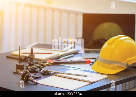 Die Ausrüstung und Dokumente des Technikteams auf den Schreibtischen im Büro sowie die gelben Helme, die beim Betreten der Baustelle getragen werden können Stockfoto