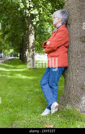 Frau, 50+, steht an einem Baum und ruht aus Stockfoto