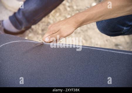 Ein kleiner Junge auf den Knien klebt das Griptape in Begleitung von Freunden bei sonnigem Wetter auf ein Skateboard. Vorbereitung eines Skateboards für einen Skatepark-Wettkampf Stockfoto