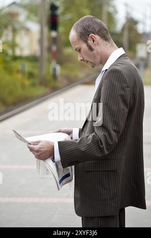 Junger Mann, der auf der Plattform steht und eine Zeitung liest Stockfoto