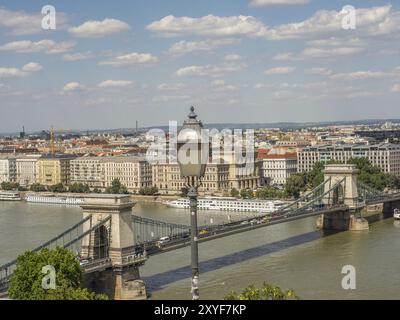 Blick auf die Stadt mit Fokus auf eine Straßenlaterne, eine Brücke über einen Fluss und viele Gebäude unter einem bewölkten Himmel, budapest, donau, ungarn Stockfoto