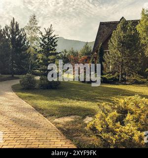 Gemütliches Landhaus aus Holz auf grüner Wiese gelegen und am sonnigen Tag von Bäumen umgeben Stockfoto