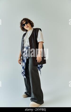 Eine Frau mit schwarzer Weste und weiträumiger Hose posiert vor weißem Hintergrund. Stockfoto