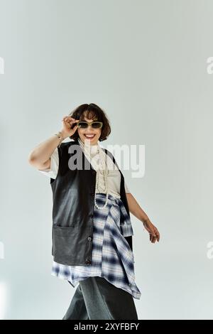 Eine junge Frau in schwarzer Lederweste und kariertem Hemd lächelt hell und passt ihre Sonnenbrille an. Stockfoto