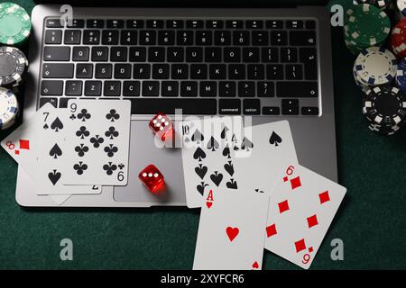 Laptop, Pokerchips, Würfel und Spielkarten auf grünem Tisch, oben Ansicht. Online-Spiel Stockfoto