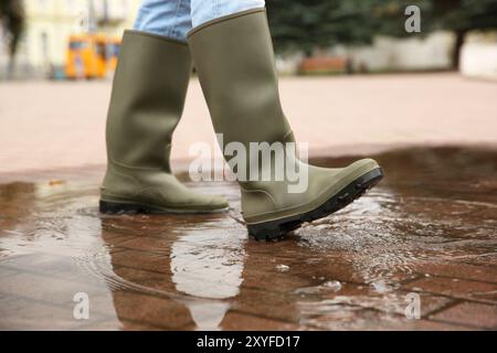 Frau mit Gummistiefeln, die draußen in der Pfütze läuft, Nahaufnahme Stockfoto