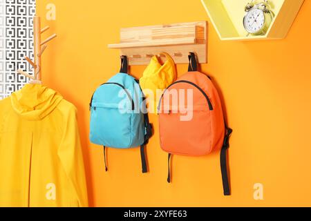 Helle Rucksäcke, Kappe, Mantel und Wecker in der Nähe der orangefarbenen Wand Stockfoto
