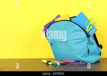 Rucksack mit anderem Schulpapier auf Holztisch vor gelbem Hintergrund Stockfoto