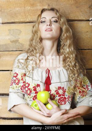 Frau in traditioneller Kleidung, die Äpfel in ihren Händen hält. Hölzerne Hintergrund Stockfoto