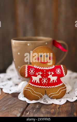 Lächelnde weihnachts-Lebkuchenmänner und Teetasse auf hölzernem Hintergrund Stockfoto