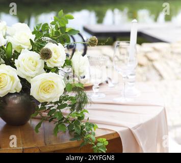 Kerzen und Vase mit weißen Rosen auf einem runden Tisch in der Nähe von Weingläsern während eines romantischen Datums im Garten Stockfoto