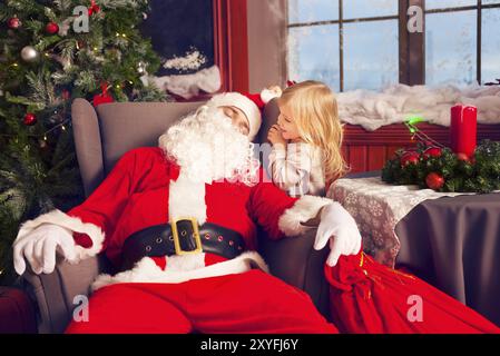 Foto von glücklichen kleinen lächelnden Mädchen Blick auf schlafenden Weihnachtsmann mit großen Beutel von Geschenken Stockfoto