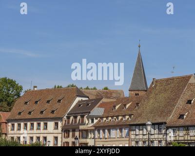 Reihe traditioneller Häuser in der Altstadt mit Fachwerkhäusern, Ziegeldächern und Kirchturm unter klarem blauem Himmel, Weissenburg, Elsass Stockfoto