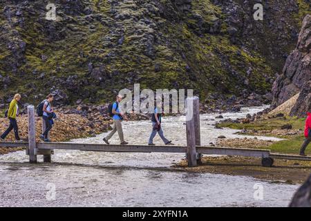 LANDMANNALAUGAR, ISLAND, 09. JULI: Einige Touristen überqueren am 09. Juli 2013 einen Fluss auf einer Holzstege in Landmannalaugar, Island, Europa Stockfoto