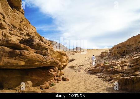 Mann in weißer arabischer Kleidung läuft in einem bunten Canyon in Ägypten Dahab Stockfoto