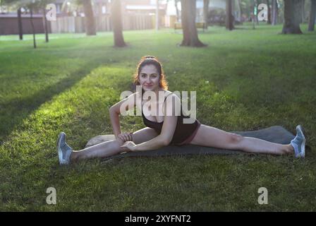 Dehnende Frau in Outdoor-Übung lächelnd glücklich, Dehnübungen nach dem Laufen zu machen. Wunderschönes, fröhlich lächelndes Sport-Fitness-Modell draußen bei Sonnenuntergang im Sommer Stockfoto