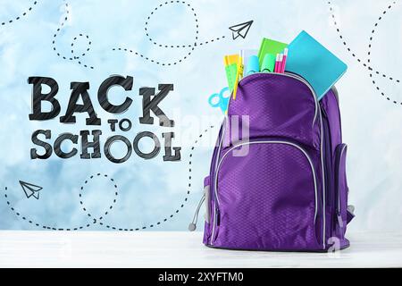 Rucksack mit Schreibwaren auf dem Schreibtisch vor hellblauem Hintergrund. Zurück zur Schule Stockfoto
