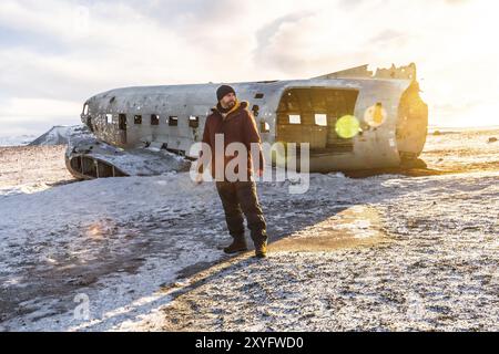 Ein Tourist, der im Winter in Island auf dem gefrorenen Solheimasandur-Strand auf dem abgestürzten Flugzeug spaziert Stockfoto