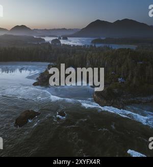 Ruhige Aussicht auf eine Meeresküste mit felsigen Küsten, dichtem Wald und fernen Bergen in der Abenddämmerung, Tofino, BC, Kanada, Nordamerika Stockfoto