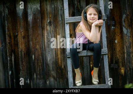 Ein Teenager mit Kopfhörern sitzt auf einer Holztreppe auf einer Farm. Stockfoto