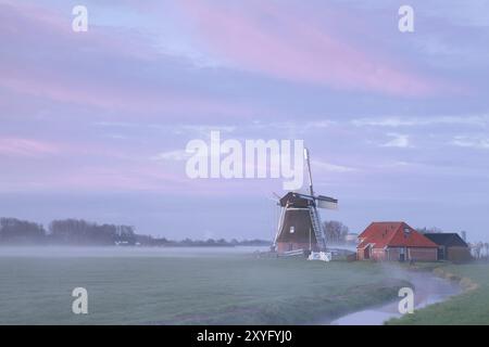 Alte Windmühle im Sonnenaufgang Nebel am Fluss, Niederlande Stockfoto