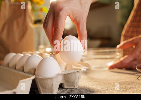 Hand nimmt Hühnerei aus der Box auf dem Küchentisch Nahaufnahme gegen Küchenatmosphäre Stockfoto