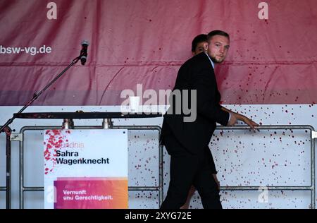 Erfurt, Deutschland. August 2024. Sahra Wagenknecht, Vorsitzende der Allianz Sahra Wagenknecht (BSW), wird nach einem Angriff mit roter Farbe während der Wahlkampagne auf dem Domplatz von einem Leibwächter von der Bühne begleitet. Am 1. September 2024 wird in Thüringen ein neuer landtag gewählt. Quelle: Martin Schutt/dpa/Alamy Live News Stockfoto