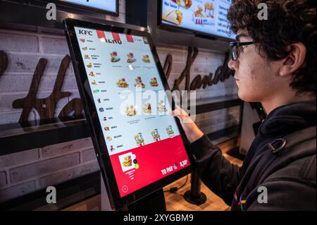 Wien, Österreich, 23. August 2022. Aufnahme der Anzeige für die unabhängige Auftragserteilung in einem kfc-Geschäft. Der Junge benutzt seinen Finger, um den Bildschirm zu berühren und zu mak Stockfoto