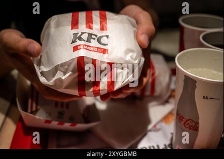 Wien, Österreich, 23. August 2022. Nahaufnahme der kfc-Sandwichfolie. Die Hand hält das Sandwich neben dem Glas Koks. Fastfood in einem großen Unternehmen Stockfoto