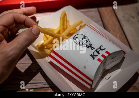 Wien, Österreich, 23. August 2022. Nahaufnahme von kfc Pommes frites und Sandwichpackung. Die Hand hält das Sandwich, die Chips sind in der Pappschachtel mit Stockfoto