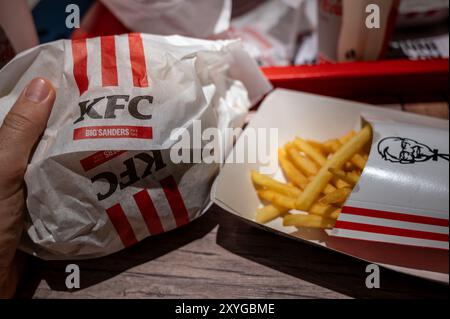 Wien, Österreich, 23. August 2022. Nahaufnahme von kfc Pommes frites und Sandwichpackung. Die Hand hält das Sandwich, die Chips sind in der Pappschachtel mit Stockfoto