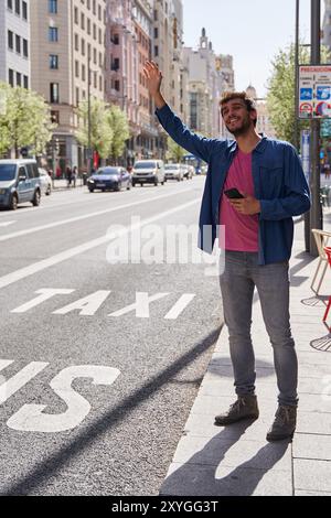 Junger hispanischer Mann hält mit erhobener Hand auf der Straße ein Taxi an. Vertikale Aufnahme Stockfoto
