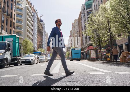 Junger Mann in lässiger Kleidung, der eine Straße an einem Straßenübergang überquert. Stockfoto