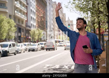 Junger hispanischer Mann hält mit erhobener Hand auf der Straße ein Taxi an Stockfoto