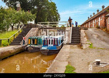 Schmalboote, die durch die Doppeltreppenschleusen auf dem Shropshire Union Kanal bei Bunbury Cheshire fahren, mit Blick auf die historischen denkmalgeschützten Ställe Stockfoto