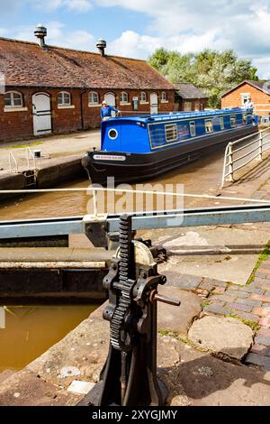 Schmalboot, das durch die Doppeltreppenschleusen auf dem Shropshire Union Kanal bei Bunbury Cheshire fährt, mit Blick auf die historischen denkmalgeschützten Ställe Stockfoto