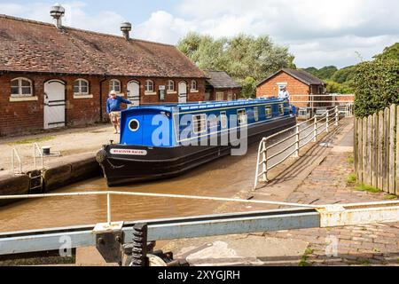 Schmalboot, das durch die Doppeltreppenschleusen auf dem Shropshire Union Kanal bei Bunbury Cheshire fährt, mit Blick auf die historischen denkmalgeschützten Ställe Stockfoto