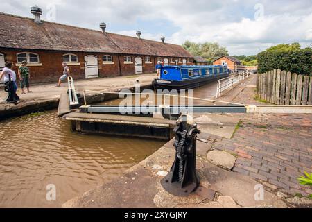 Schmalboot, das durch die Doppeltreppenschleusen auf dem Shropshire Union Kanal bei Bunbury Cheshire fährt, mit Blick auf die historischen denkmalgeschützten Ställe Stockfoto